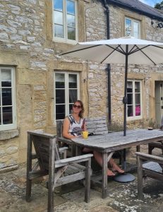 Vrouw geniet van een kopje thee onder een parasol voor een Engelse cottage – moment van rust en zelfzorg in de buitenlucht.