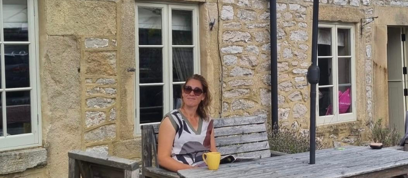 Vrouw geniet van een kopje thee onder een parasol voor een Engelse cottage – moment van rust en zelfzorg in de buitenlucht.